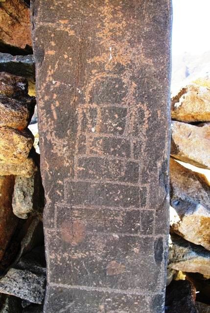 Fig. 8. A close-up of the upper chorten on the pillar reveals more complexity. It is now composed of five sharply incised graduated tiers, which sit on a tall plinth and are topped by a small semi-circular bumpa. The bumpa appears to be surmounted by a segmented spire, which is more heavily patinated and carved in a different manner (using a pecking technique). In fact, this spire, and the bumpa and two of the tiers below it appear to constitute an older and cruder petroglyph. The remainder of the current one was almost certainly added on later using more sophisticated cutting tools. The relative degree of physical wear indicates that possibly centuries separate the creation and recreation of this petroglyph. On the basis of the style and carving technique, the earlier part of the upper chorten, lower chorten (with its three crude tiers and bumpa) and swastika can probably be attributed to the early historic period (650–1000 CE). The more recent portion of the upper chorten dates to the vestigial period (1000–1250 CE) or perhaps even later. The clockwise orientation of the swastika may possibly indicate a Buddhist identity for it and the other carvings as well. 