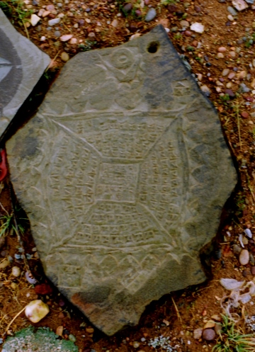 Fig. 3. The stone plaque is organized similarly to fig. 2, however, surrounding each of the four quarters of kha syllables is a line of mountains (three rows contain eight peaks and the other row six peaks for a total of 30 mountains). Two of the names of the four warrior spirits (lion and horned eagle) are still intact. The other two are now missing. These four deities are closely aligned to mountains, probably helping to explain the inclusion of peaks in the carvings. At the top of the image is the conjoined sun and moon (nyi-zla), a cardinal symbol of Tibetan Buddhism (signifying the union of wisdom and compassion, the means to enlightenment). Tshochen/Gertse.