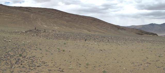 Fig. 18. The stelar necropolis near Thangde Mukyu viewed from the south. Note how the entire site is cloaked in rubble. Some of the small stelae or pillars of the array are visible in the middle of the photograph. Three mounds behind the rock strewn terrain are discernable. From left to right they are the temple-tomb (Mound I), companion structure (Mound II), and the most northeasterly structure at the site (Mound III). Like the temple-tomb, Mound II and Mound III appear to have been burial structures that stood conspicuously above the ground. The mountain range to the west seen in the photograph comes within 1 km of the site.