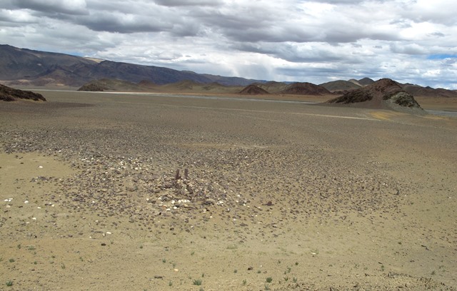 Fig. 20. The stelar necropolis viewed from the top of a small outcrop situated a few meters southwest of the site. The temple-tomb and array of stelae is in the foreground. Note how the terrain around these monuments is blanketed in rubble, much of which appears to have once been an integral part of the complex.