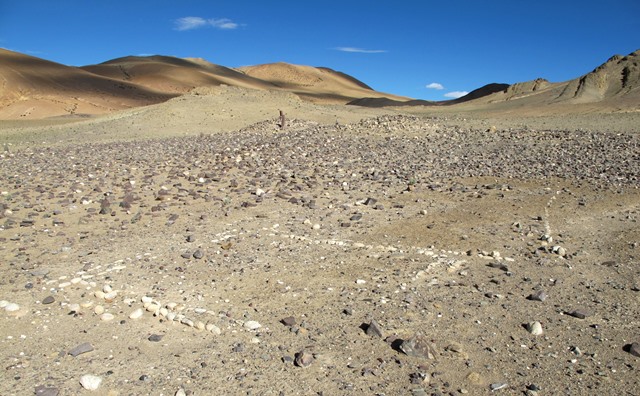 Fig. 21. The site from the northeast with white cobble enclosure in the foreground. Enclosures of various types at stelar necropolises were variously used for ritual and burial purposes. Note the light-colored natural outcrop situated 10 m southwest of the temple-tomb (mound with pillars sticking out).
